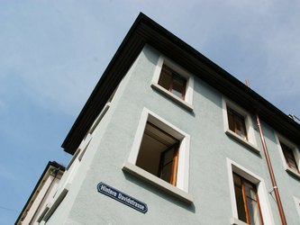 Bild eines Gebäudes mit blauem Strassenschild „Hintere Davidstrasse“ unter einem klaren Himmel.
